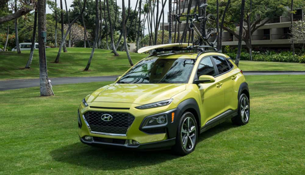 Lime green Hyundai Kona with surfboard on roof rack parked on grass