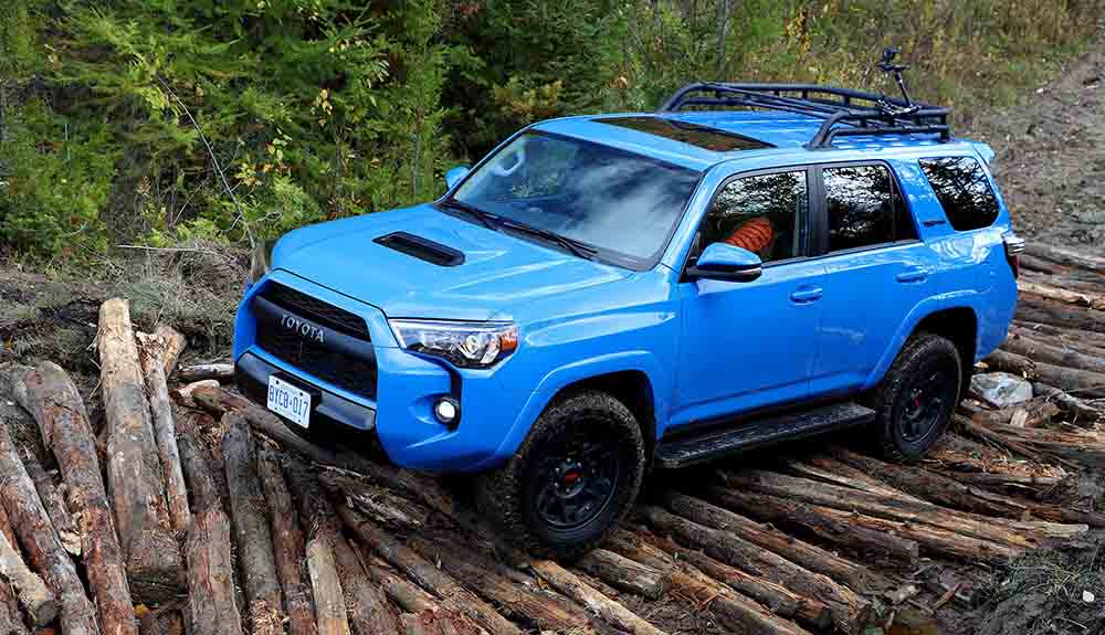 Blue Toyota 4Runner driving over a stack of logs in the forest
