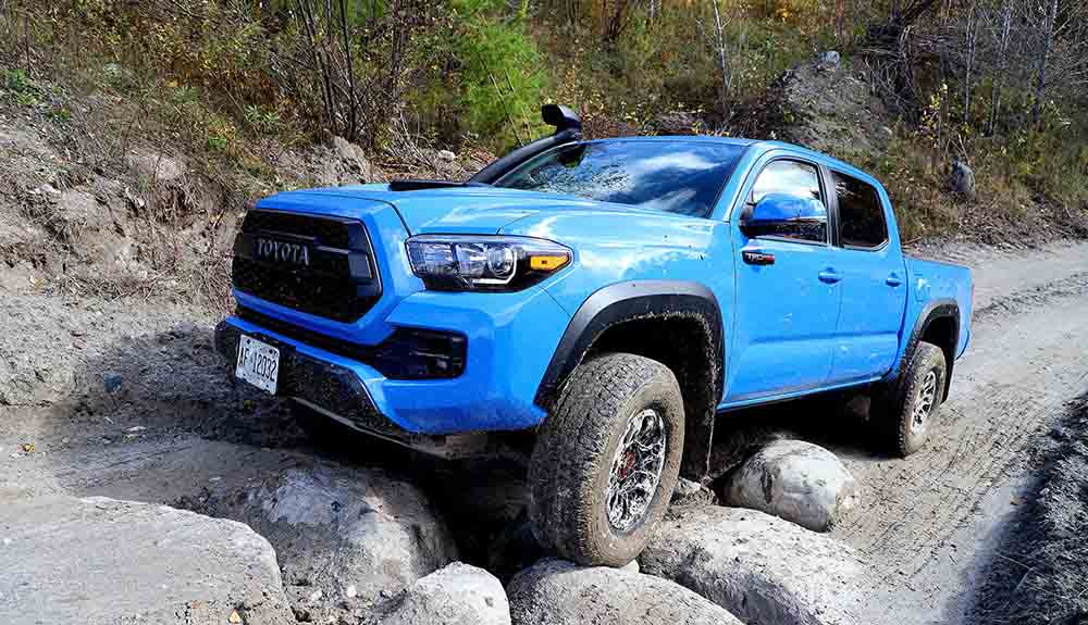 Blue Toyota Tacoma driving up a hill of rocks on a dirt road 