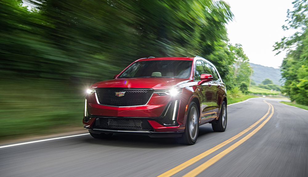 A red Cadillac XT6 drives on a tree-lined road