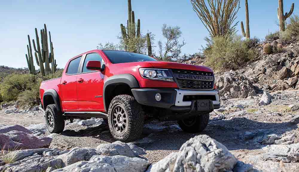 Red Chevy Colorado pickup truck driving over rocks