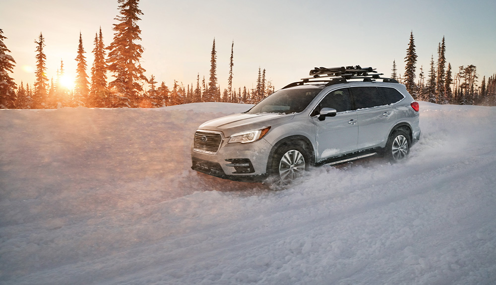 A white Subaru Ascent drives through the snow.