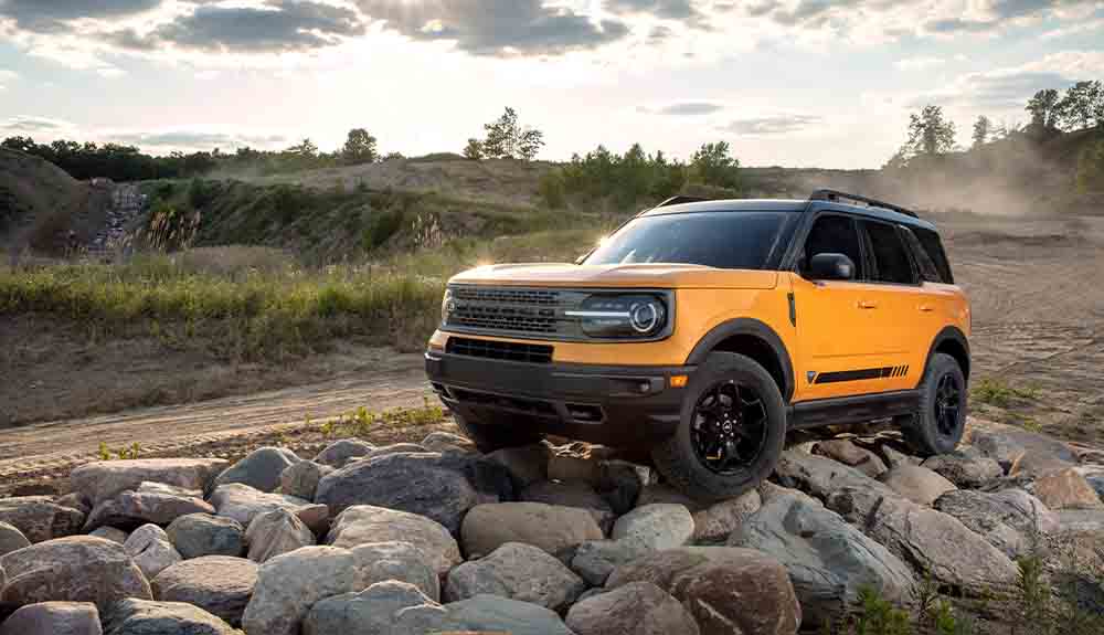 A yellow 2021 Ford Bronco is parked on rocks off a dirt road