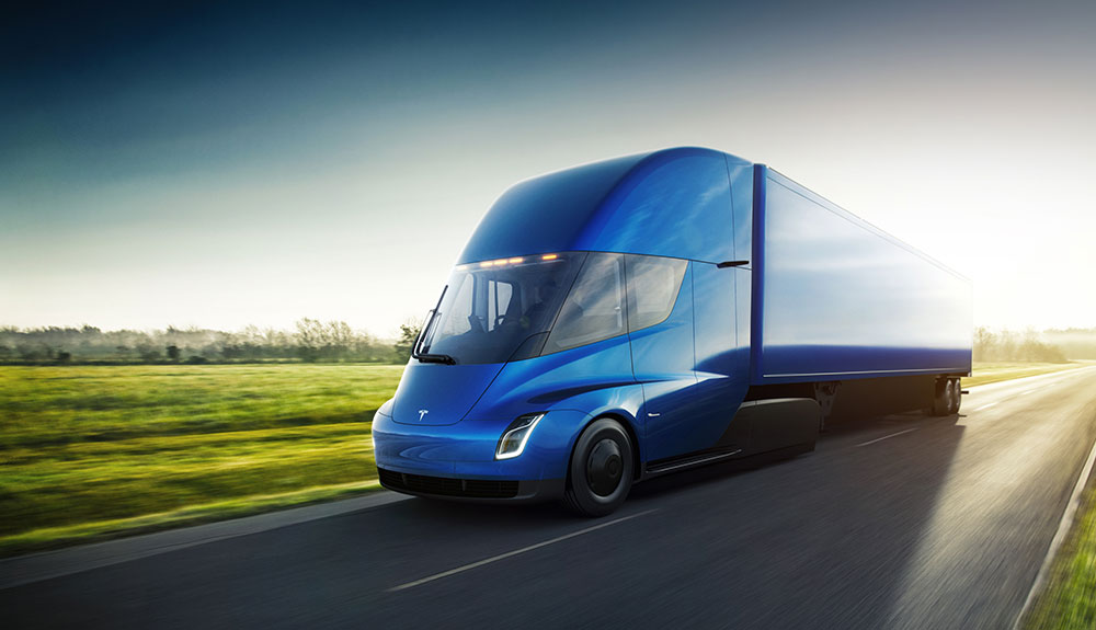 Gleaming, clean-looking bright blue Tesla Semi truck speeding down empty freeway with grass blurred in background