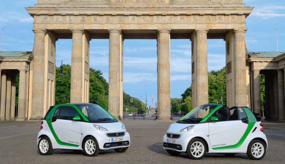 Two tiny Smart Fortwo parked outside an archway with a European vibe