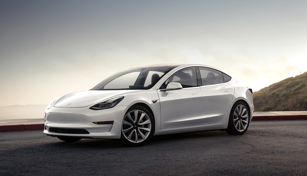 Light silver Tesla Model 3 shining in the bright light beside waterfront