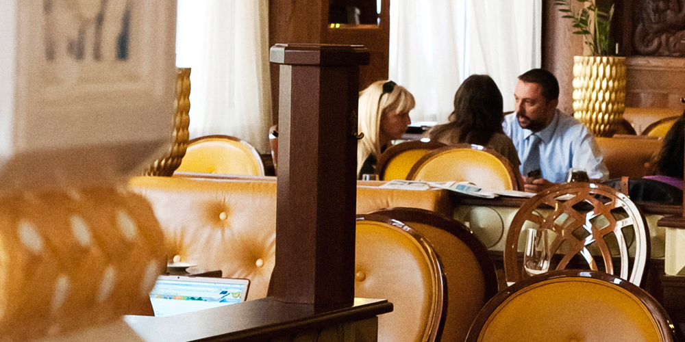 Three people sit talking in a luxurious Prague restaurant, leather chairs and dark wooden furniture throughout