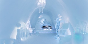 The carved ice interior of an ice hotel, ice scuptures seen around the room and a chandelier made of ice sparkles from the ceiling