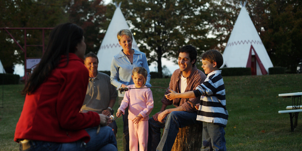 A family roasts marshmallows and warms up around a campfire at Wigwam Village in Kentucky, two wigwams behind them