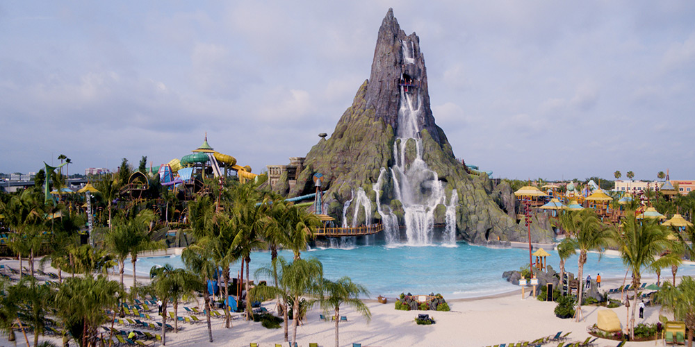 A large waterfall flows into a blue pool lined with palm trees at Universal Orlando Resort