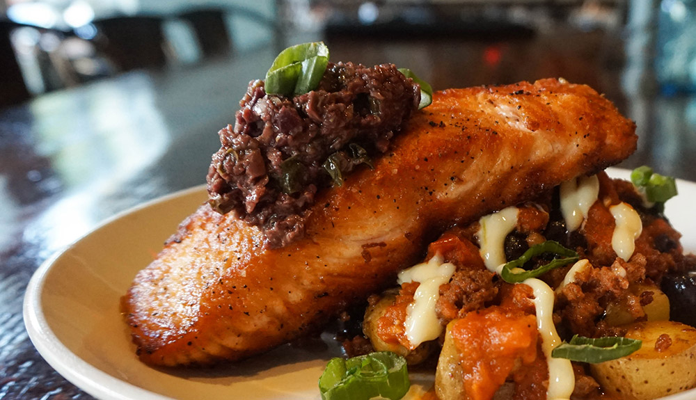 An appetizing plate with fish fillet topped with a chutney, on aioli-drizzled potatoes
