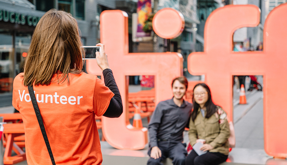 TIFF volunteer captures a photo of man and woman by the 'TIFF' sign on King Street West