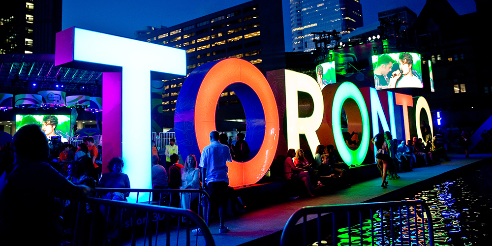 The Toronto sign lit up at night surrounded by lots of people in downtown Toronto