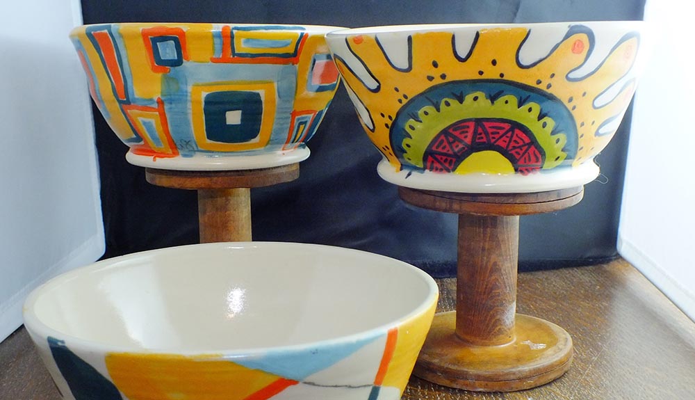 Three painted bowls featuring various patterns using light oranges, blues, greens and pink