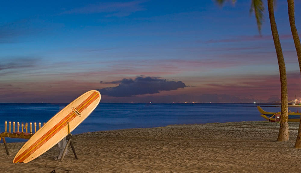 A lone surfboard is stacked on a wooden stand at sandy Waikiki beach at night