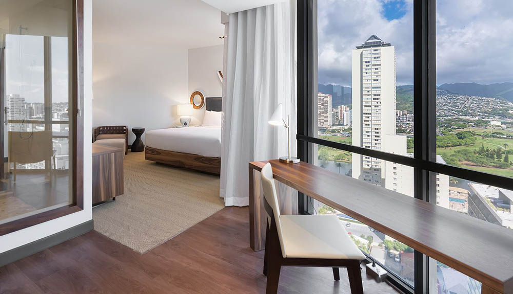 A large hotel room with seating area and large bedroom is seen, the window looking out at the city in the Hyatt Centric Waikiki Beach, Oahu