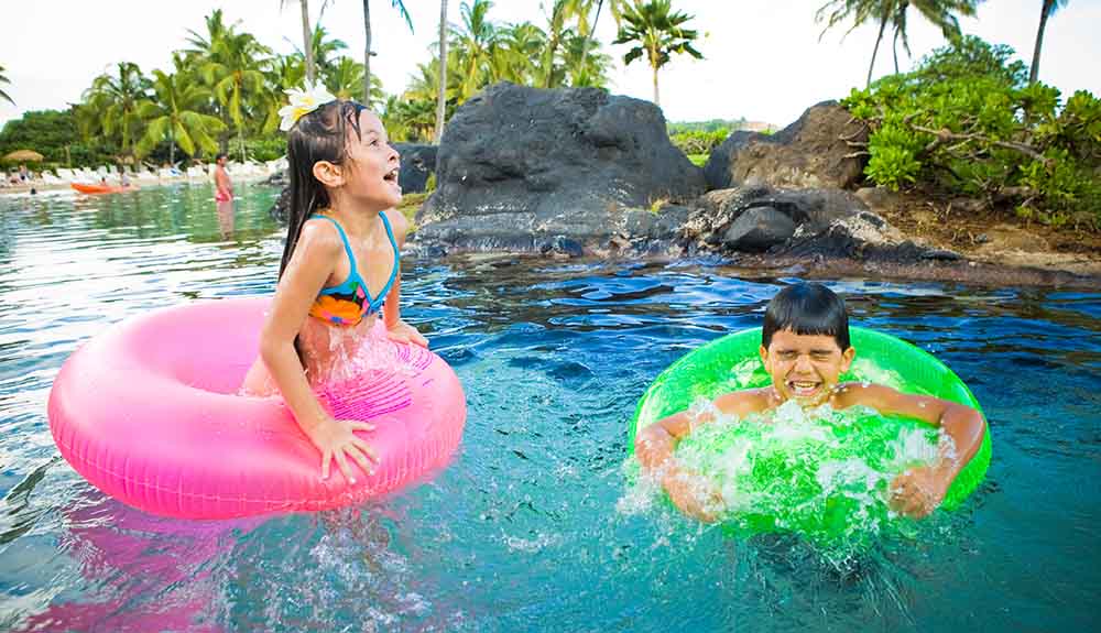 Two children wearing bright pool floaties splash in the pool at the Grand Hyatt Kauai Resort and Spa in Kauai