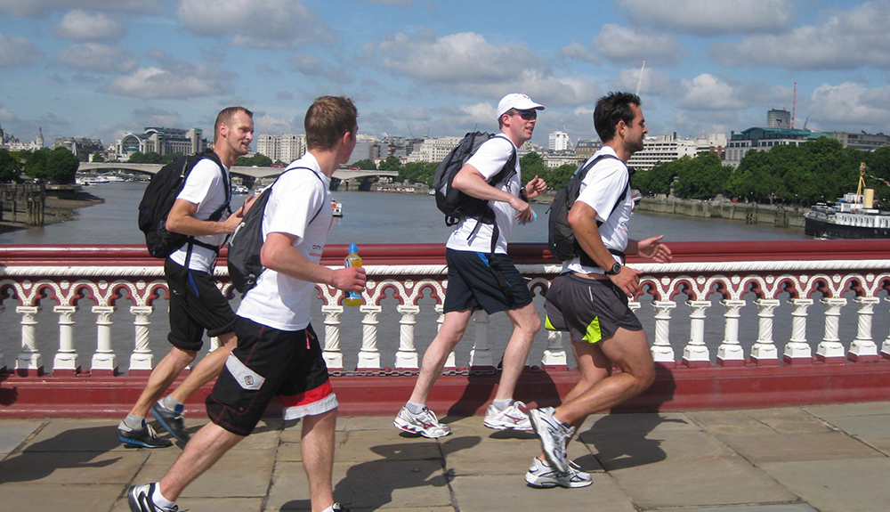 Four men in white shirts and shorts run along the River Thames in London