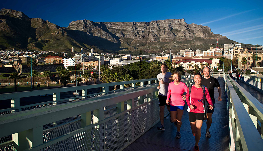 Four adults run across a narrow bridge in Capetown
