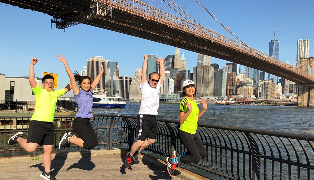 Four people dressed in athletic wear run beneath the Brooklyn Bridge