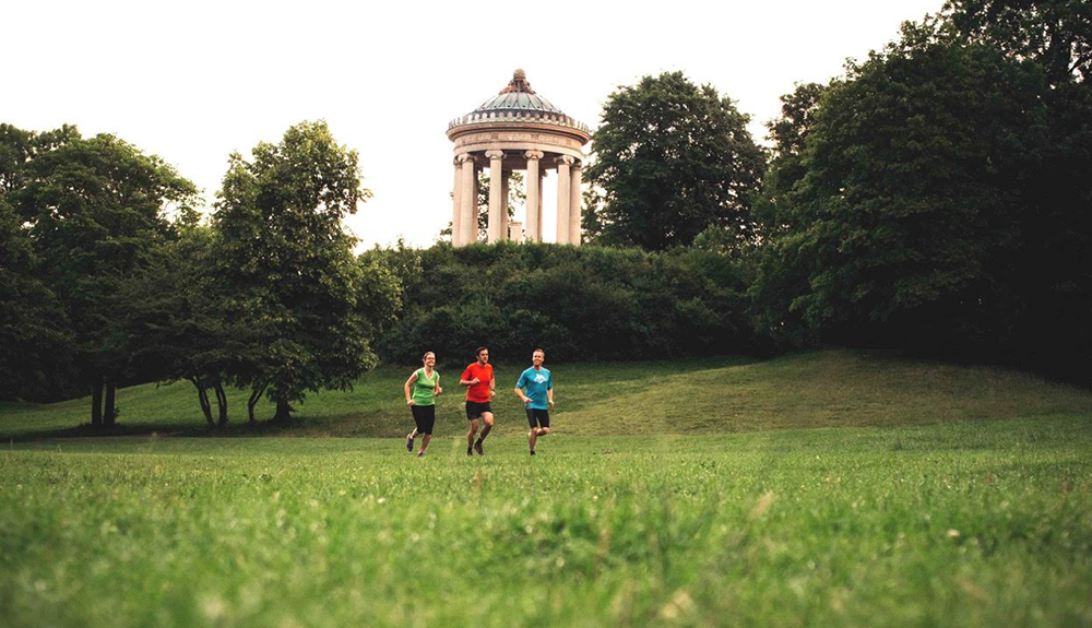 Three people run across grass in Munich