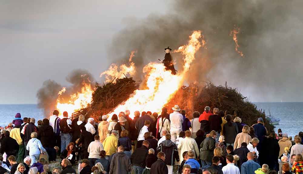 A witch rides a broom on the top of burning sticks on a beach in Denmark