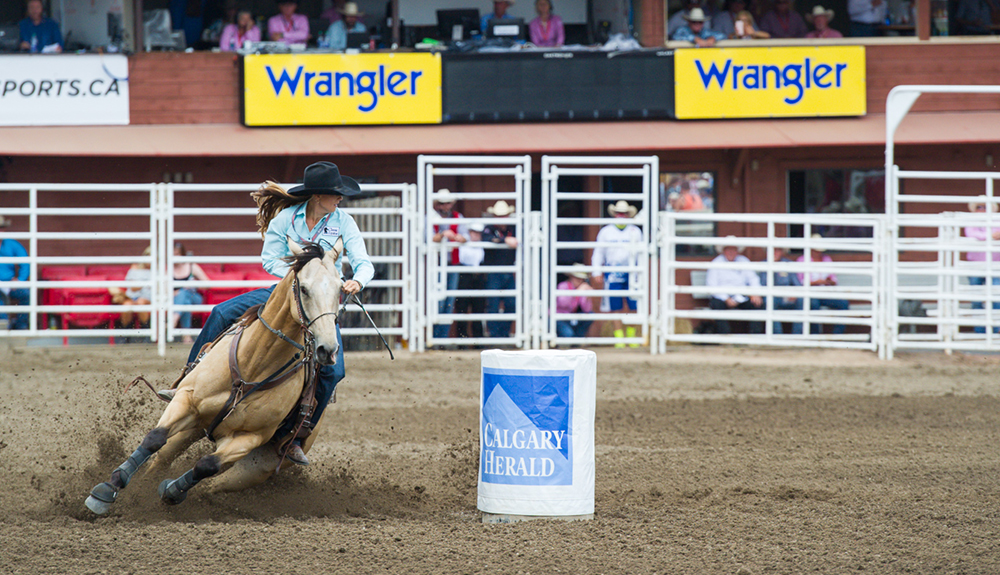 Equestrian wearing a cowboy hat rides low as a horse takes a sharp turn