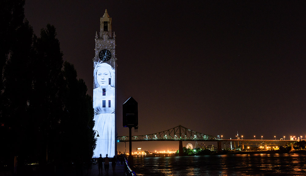 An image of a woman is projected on to a tower in Old Montreal at night for the Cite Memoire experience