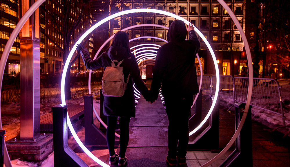 A couple walks through wings of light while holding hands as they take in the romantic Montreal en lumiere