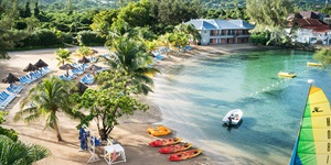 Clear waters are seen at a sandy beach, various boats at the ready and lounge chairs lined up for a day of fun in the sun