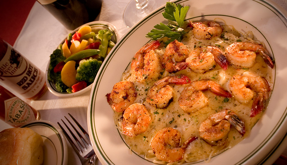 A diner of shrimp and grits with a side of vegetables and hot sauce