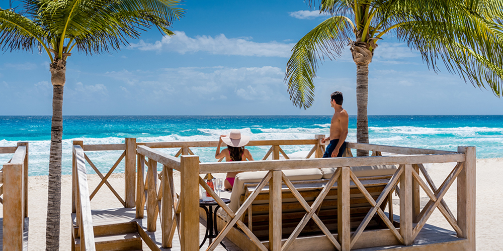 A man and woman enjoy the beach view from a wooden viewpoint in Cancun