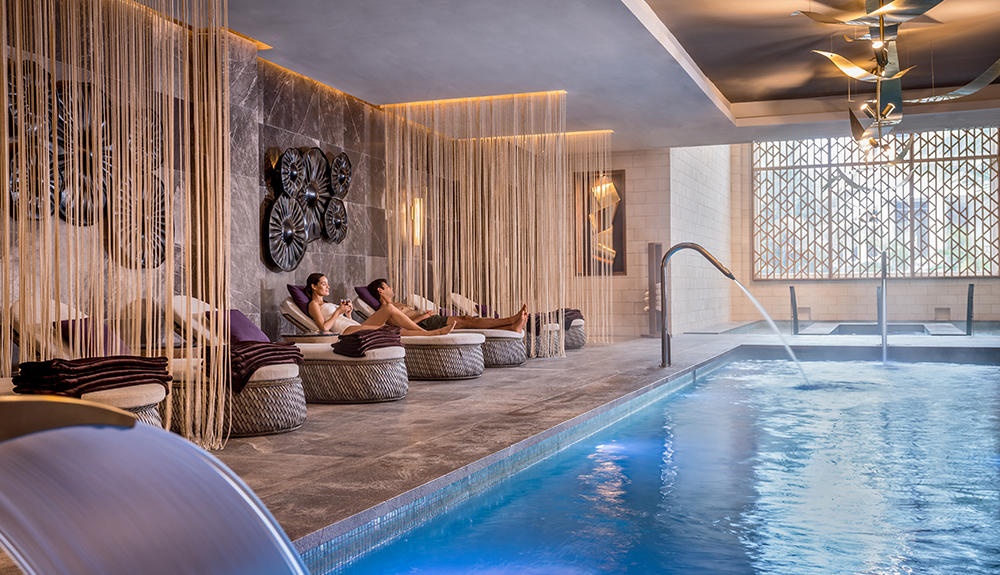 Woman and man sit on individual loungers by the indoor pool in the Zen Spa