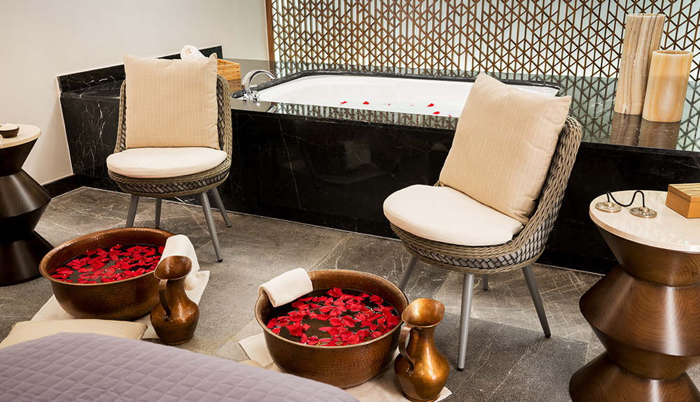 Two chairs with cushions with buckets of water with rose petals in it at the foot of them