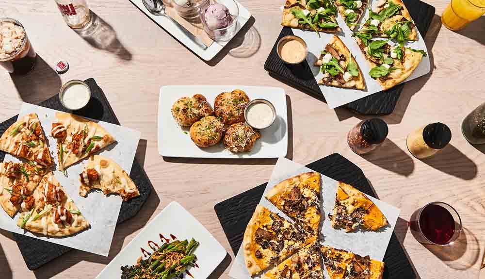 Pizza cut up in pieces on square plates and other food on offer