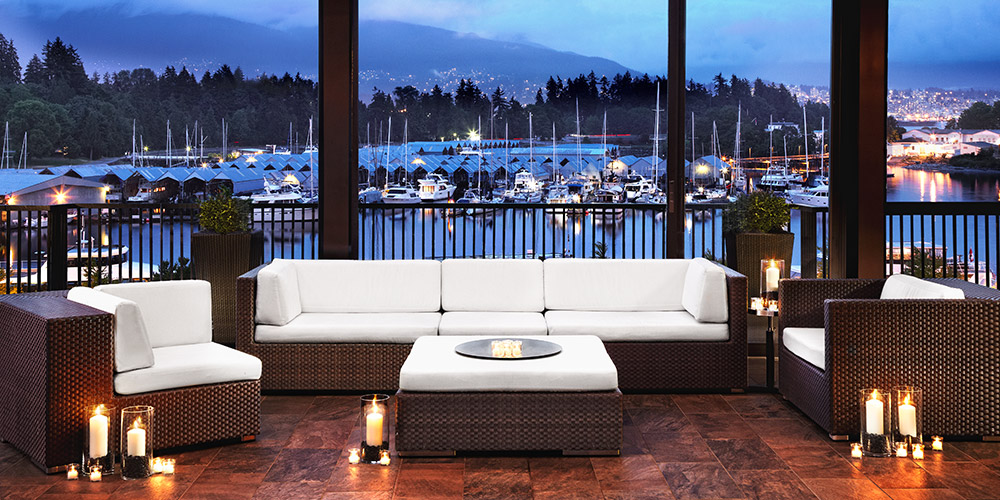 A cozy rattan and white seating area is lit up with candles at a Canadian hotel, a harbourfront seen outside the window