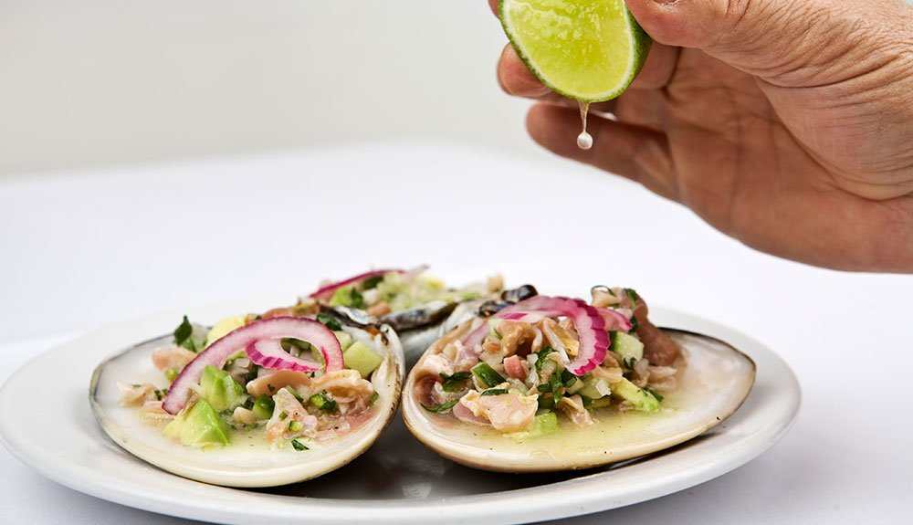 Three shells filled with delicious seafood being sprinkled with fresh lime juice from a lime wedge