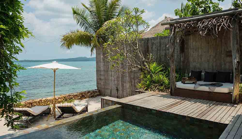 Private pool with deck, outdoor bed in a cabana next to private beach with two loungers on the sand