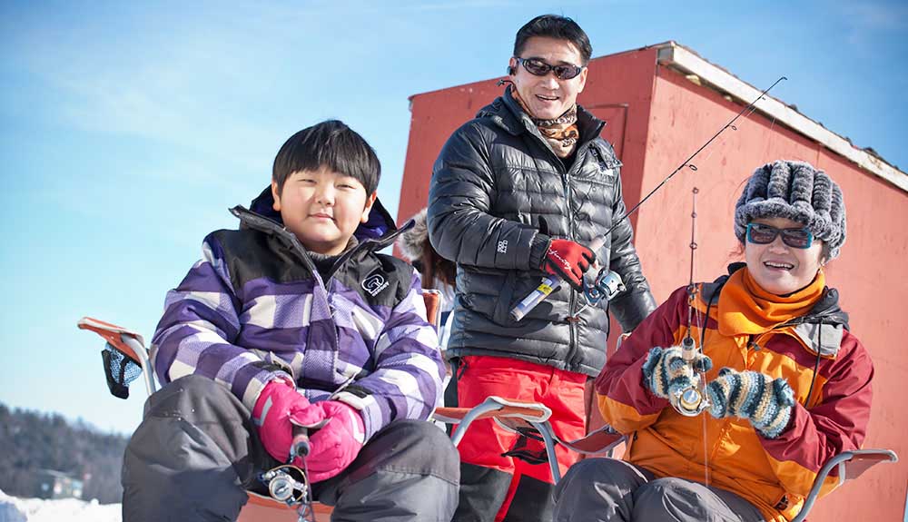 Asian boy, Asian man and Asian woman wearing winter coats, holding fishing rods enjoying fishing in the winter