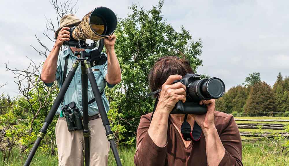 Man looking through a telescope and woman snapping photos as they birdwatch together