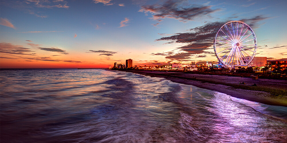 Myrtle Beach and Ferris wheel seen from the edge of the water at sunset