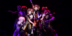 A group of cast members from the musical CATS on stage lit by red and purple lighting
