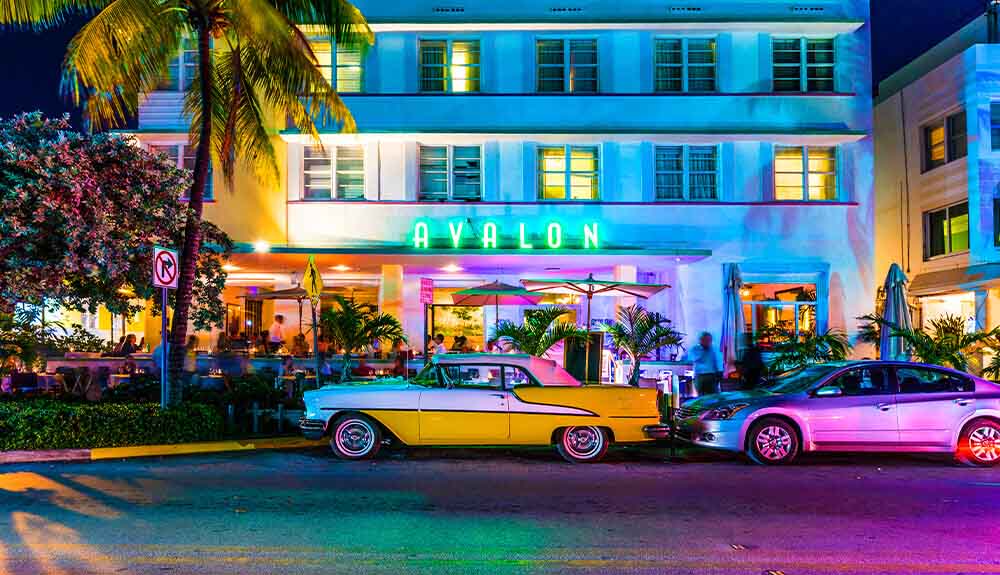 A classic car and a modern car are parked out front of the Avalon Hotel in Miamia