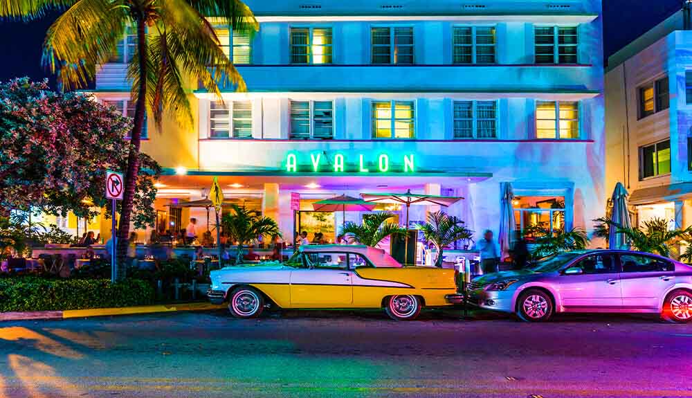 A classic car and a modern car are parked out front of the Avalon Hotel in Miamia