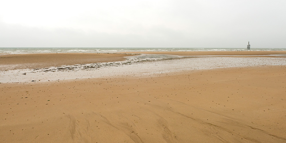 A wide expanse of Juno Beach in France is shown on a cloudy day