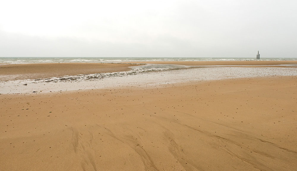 A wide expanse of Juno Beach in France is shown on a cloudy day