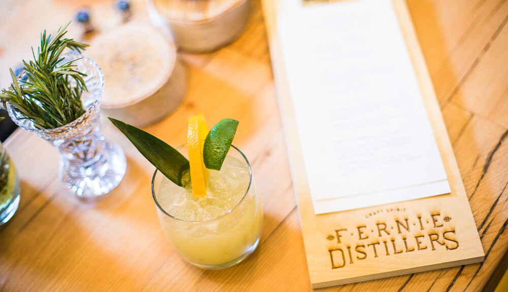 Drink menu and cocktail garnished with lemon slice on table at Fernie Distillers in Fernie, B.C., Canada