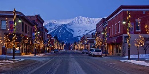 Looking toward red brick buildings, trees strung with lights and snowy mountains in the distance on Main Street in Fernie, B.C., Canada