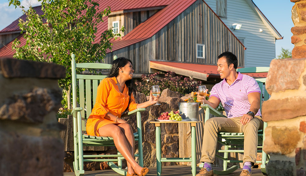 A man and woman sit on an outdoor patio set drinking wine and laughing