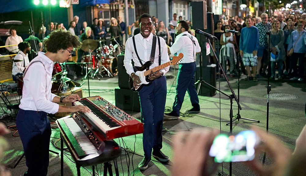 A male musician plays the keyboards while another man holds a guitar on stage at the Beaches International Jazz Festival in Toronto